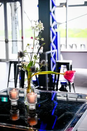 Two candles and a tall white and green floral arrangement atop a high black table.