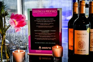 Cocktail and mocktail menu atop a black bar adorned with florals, candles, and wine bottes.