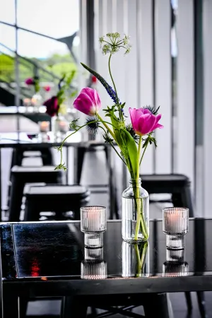 Closeup of a well-lit floral magenta floral arrangement, in a vase, flanked by candles, atop a black table.