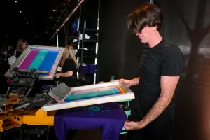 A man using the t-shirt printing press to print a purple t-shirt for a guest.