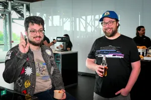 Two glasses-wearing male guests smile and pose together with their food and drink.