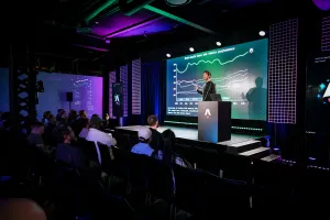 Fred K. Schott on stage in front of a slide depicting a graph, standing next a podium with a laptop sitting atop it. Wide shot including the audience.