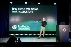 Ben Holmes on stage gesturing to the slide behind him that says, "It is time to take astro:action."