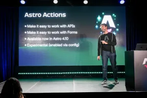 Fred K. Schott speaking on stage, pointing off-stage at the audience. Behind him is a summary of Astro Actions on the LED screen.