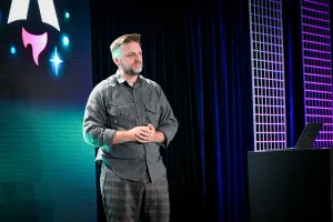 Matthew Phillips speaking on stage next to a podium with a laptop on it. Behind him is the Astro Together logo on-screen.