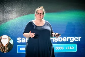 Sarah Rainsberger on stage, introducing herself. Her right hand gestures towards the audience while the left holds a clicker.