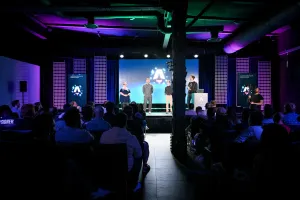 View from the back of the audience. Keynote speakers on stage. From left to right: Sarah Rainsberger, Matthew Phillips, Ben Holmes, and Fred K. Schott (next to the podium).