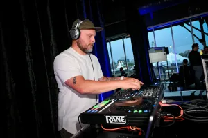 A DJ wears a cap and headphones while mixing at his booth.