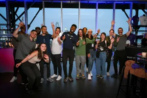 A large group of guests pose for a group photo in front of floor-to-ceiling windows.